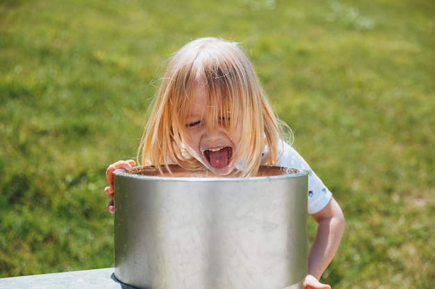 Ein kleiner blonder Junge trinkt an einem heißen Sommertag im Freien aus einem Trinkbrunnen in einem Stadtpark