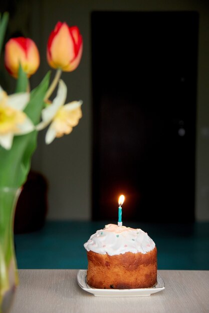 Ein kleiner festlicher Kuchen mit einer brennenden Kerze auf dem Tisch zum Geburtstag