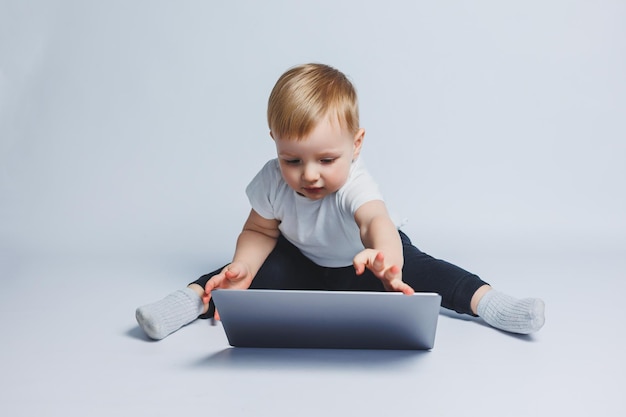 Ein kleiner Junge, 34 Jahre alt, sitzt mit einem Laptop auf weißem Hintergrund Ein Kind in einem weißen T-Shirt und einer schwarzen Hose betrachtet einen Laptop Moderne Kinder