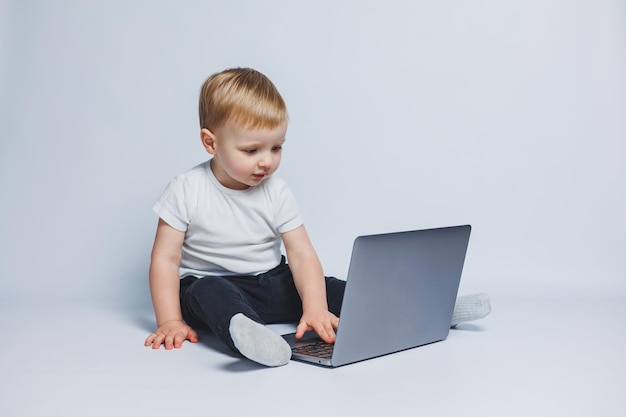 Ein kleiner Junge, 34 Jahre alt, sitzt mit einem Laptop auf weißem Hintergrund Ein Kind in einem weißen T-Shirt und einer schwarzen Hose betrachtet einen Laptop Moderne Kinder