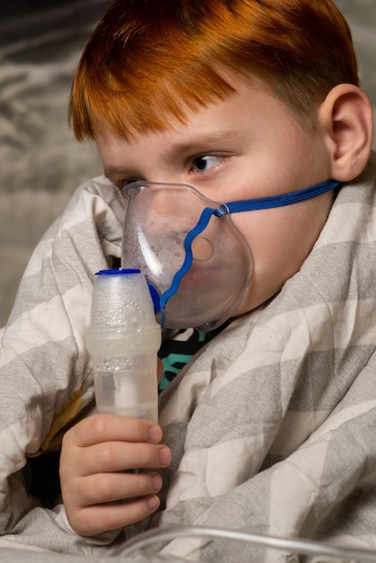 Ein kleiner Junge atmet durch einen Inhalator im Bett Baby in eine Decke gewickelt Behandlungskonzept für Bronchitis-Pneumonie-Coronavirus