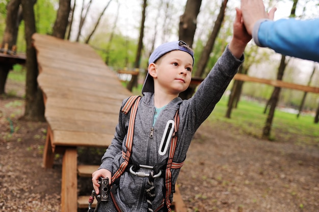 Ein kleiner Junge auf einer Attraktion in einem Seilpark passiert einen Hindernisparcours