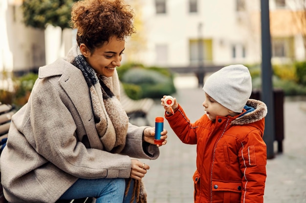 Ein kleiner Junge bläst Seifenblasen mit seinem Babysitter im Park