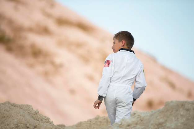 Ein kleiner Junge, der als amerikanischer Astronaut verkleidet ist, geht durch exotische Berge aus weißem Sand