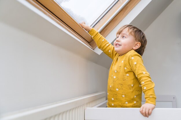 Ein kleiner Junge, der morgens in seinem Bett steht und auf das Dachfenster schaut.