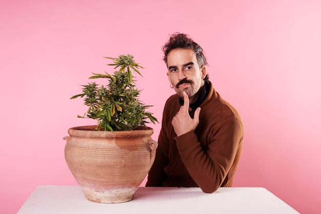 Ein kleiner Junge, der neben einer Marihuana-Pflanze mit rosa Hintergrund denkt