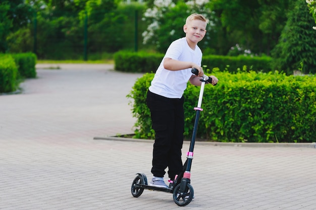 Ein kleiner Junge fährt im Sommer einen Roller im Park. Foto in hoher Qualität