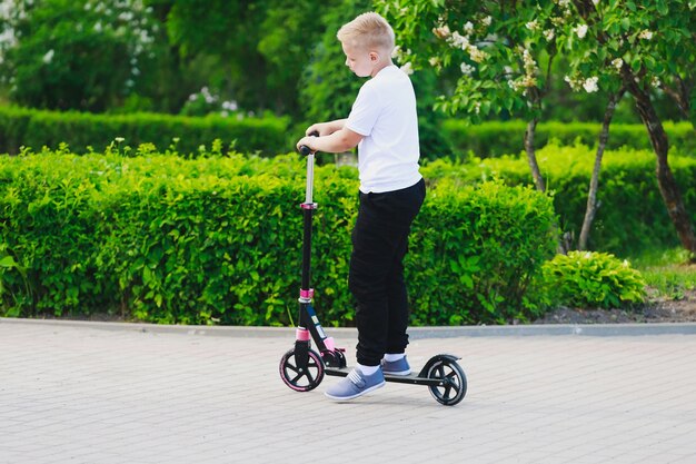 Ein kleiner Junge fährt im Sommer einen Roller im Park. Foto in hoher Qualität