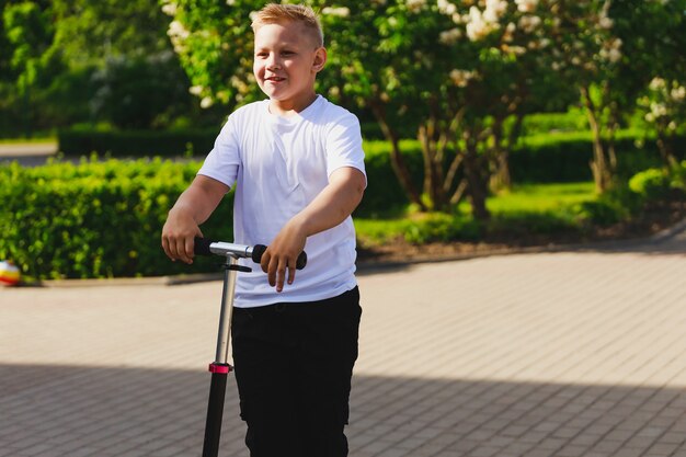 Ein kleiner Junge fährt im Sommer einen Roller im Park. Foto in hoher Qualität