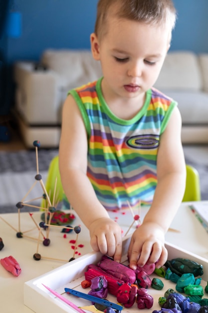 Ein kleiner Junge formt aus Plastilin am Tisch zu Hause einen Turm aus Zahnstochern und Kugeln