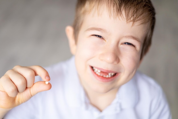 Ein kleiner Junge hält seinen ersten gefallenen Milchzahn in der Hand Das Kind wächst auf, Zähne fallen aus Pflege von Milchzähnen und Mundhöhle