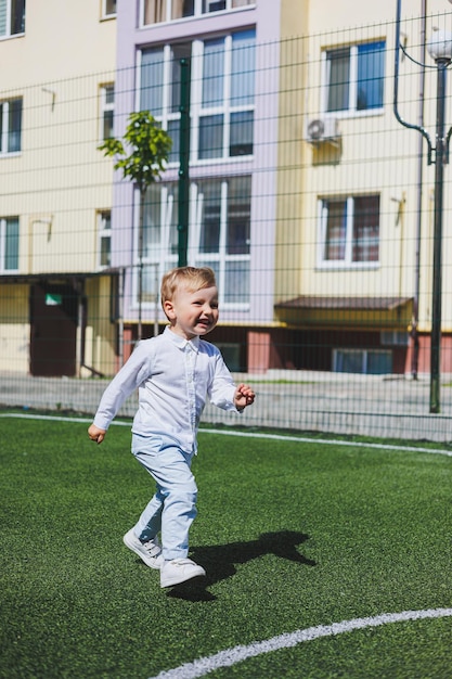 Ein kleiner Junge im Alter von 2 Jahren in Hemd und Hose läuft und lacht Ein Kind an einem sonnigen Tag freut sich und lächelt