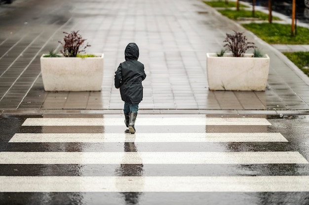 Ein kleiner Junge in Eile geht am regnerischen Tag über den Zebrastreifen