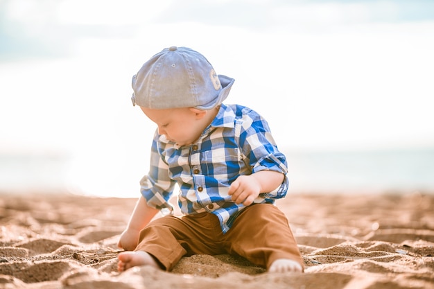 Ein kleiner Junge in einem blauen Hemd spielt am Strand mit Steinen und Muscheln