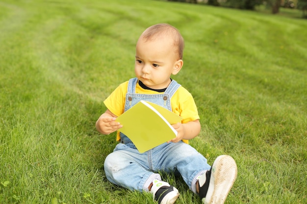 ein kleiner Junge in einem gelben T-Shirt und Jeans sitzt mit einem Notebook auf dem Rasen im Park