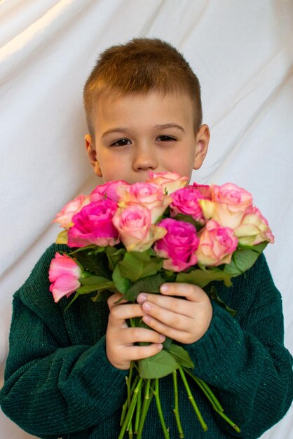 Ein kleiner Junge in einem grünen Pullover gibt einen Strauß rosa Rosen