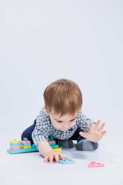 Ein kleiner Junge in einem Hemd baut ein buntes Holzspielzeug auf weißem Hintergrund Das Konzept der Entwicklungsspiele für Kinder für Kinderspielzeug Kopieren Sie Platz