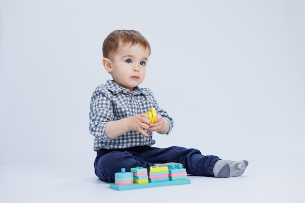 Ein kleiner Junge in einem Hemd baut ein buntes Holzspielzeug auf weißem Hintergrund Das Konzept der Entwicklungsspiele für Kinder für Kinderspielzeug Kopieren Sie Platz