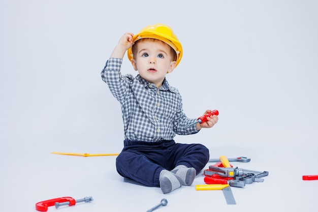 Ein kleiner Junge in einem Hemd mit einem Helm und einem Spielzeugwerkzeug Weißer Hintergrund Spielzeugkonstruktionswerkzeug für Kinder