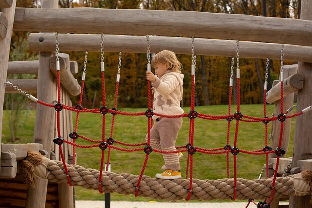 ein kleiner Junge in einem leichten, warmen Strickanzug spielt auf einer Kinderrutsche in einem Stadtpark