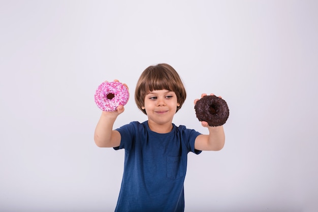 Ein kleiner Junge in einem T-Shirt hält zwei Donuts auf weißem Hintergrund mit Platz für Text