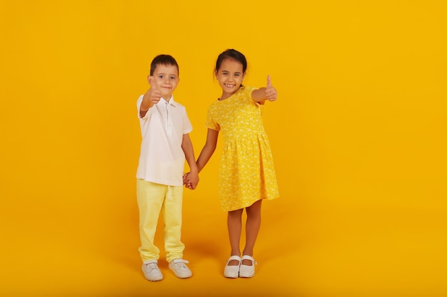 ein kleiner Junge in einem weißen T-Shirt und einer gelben Hose hält die Hand seiner Schwester in einem gelben Kleid