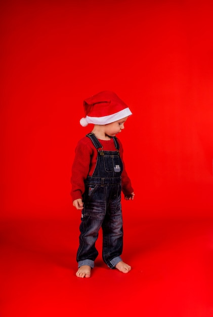 Ein kleiner Junge in Jeansoverall und Weihnachtsmütze steht seitlich