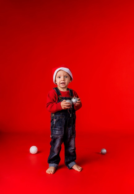 Ein kleiner Junge in Jeansoverall und Weihnachtsmütze steht