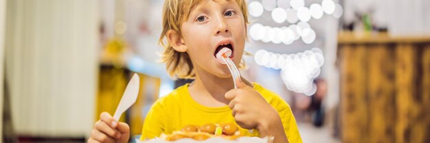 Ein kleiner Junge isst Dessertwaffeln mit Marmelade in einem Café-Banner-Langformat