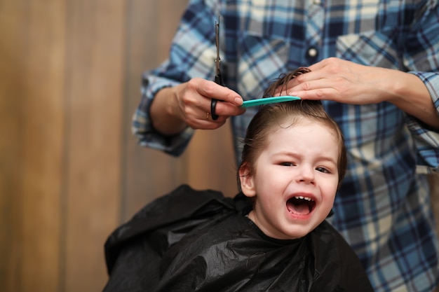 Ein kleiner Junge ist getrimmt in den strahlenden Emotionen des Friseurs auf seinem Gesicht