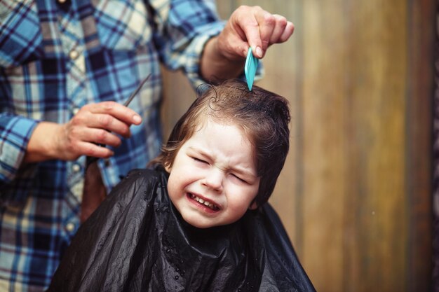 Ein kleiner Junge ist getrimmt in den strahlenden Emotionen des Friseurs auf seinem Gesicht