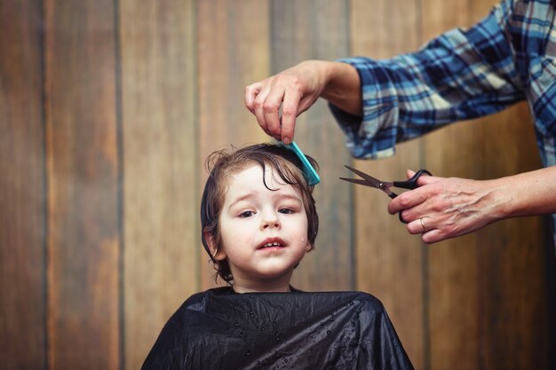 Ein kleiner Junge ist getrimmt in den strahlenden Emotionen des Friseurs auf seinem Gesicht