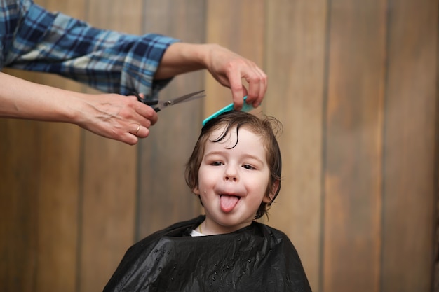 Ein kleiner Junge ist getrimmt in den strahlenden Emotionen des Friseurs auf seinem Gesicht