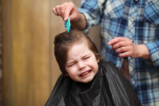 Ein kleiner Junge ist getrimmt in den strahlenden Emotionen des Friseurs auf seinem Gesicht
