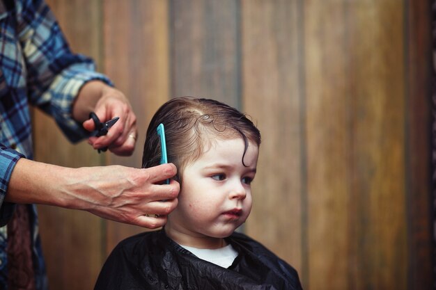 Ein kleiner Junge ist getrimmt in den strahlenden Emotionen des Friseurs auf seinem Gesicht