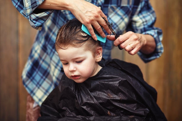 Ein kleiner Junge ist getrimmt in den strahlenden Emotionen des Friseurs auf seinem Gesicht