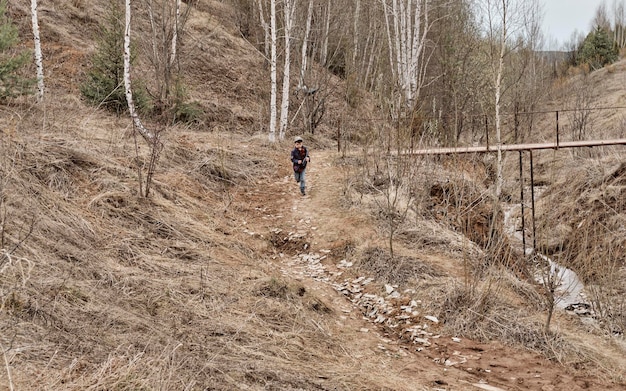 Ein kleiner Junge läuft an einem bewölkten Herbsttag vom Hügel herunter Ein Hügel mit trockenem Gras Sandweg Kindheit auf dem Land Einsamer Junge spielt