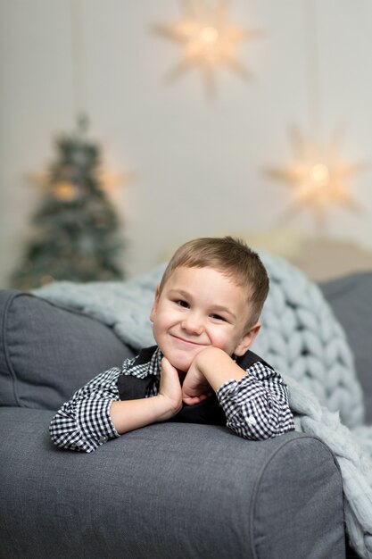 Ein kleiner Junge liegt auf einem Sofa mit einer grauen Strickdecke und lächelt.