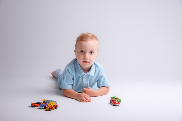 Ein kleiner Junge liegt und spielt mit Autos auf weißem Hintergrund