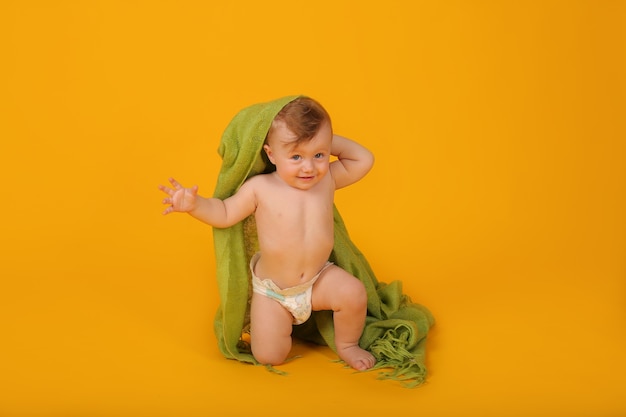 ein kleiner Junge mit blauen Augen ist mit einer grünen Decke bedeckt und sitzt auf einem gelben Hintergrund