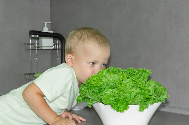 Ein kleiner Junge mit kurzem Haarschnitt hilft beim Kochen in der Küche und wäscht frisches Gemüse