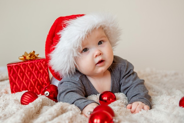 Ein kleiner Junge mit Weihnachtsmannmütze liegt auf dem Bett und spielt mit Weihnachtskugeln