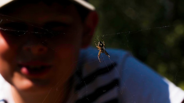 Foto ein kleiner junge schaut auf eine spinne an einem sonnigen tag kreativ ein kind in einer mütze schaut auf ein insekt, das sitzt