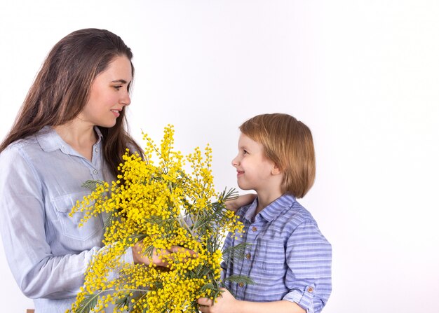 Ein kleiner junge schenkt seiner mutter einen frühlingsstrauß mit gelber mimose. herzlichen glückwunsch zum muttertag, dem 8. märz.