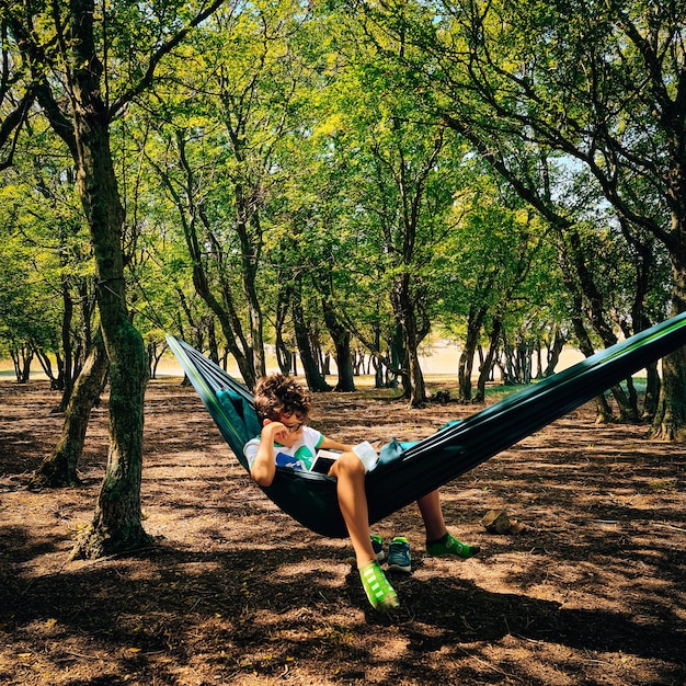 Ein kleiner Junge sitzt im Park auf einer Hängematte.