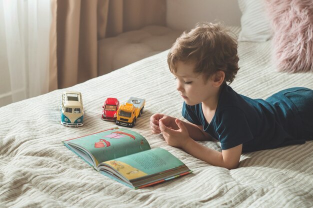 Ein kleiner Junge sitzt mit einem Buch auf einem Bett