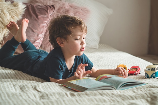 Ein kleiner Junge sitzt mit einem Buch auf einem Bett