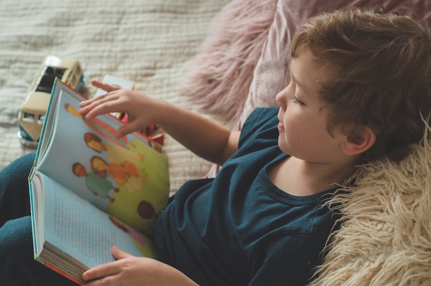 Ein kleiner Junge sitzt mit einem Buch auf einem Bett