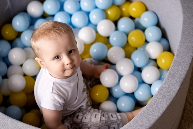 ein kleiner junge sitzt und spielt in plastikbällen. das Kind lächelt