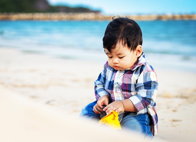 Ein kleiner Junge spielt am Strand und trägt ein Flanellhemd